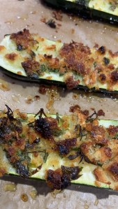 Baked zucchini halves topped with a crispy breadcrumb mixture, arranged on a parchment-lined baking tray.